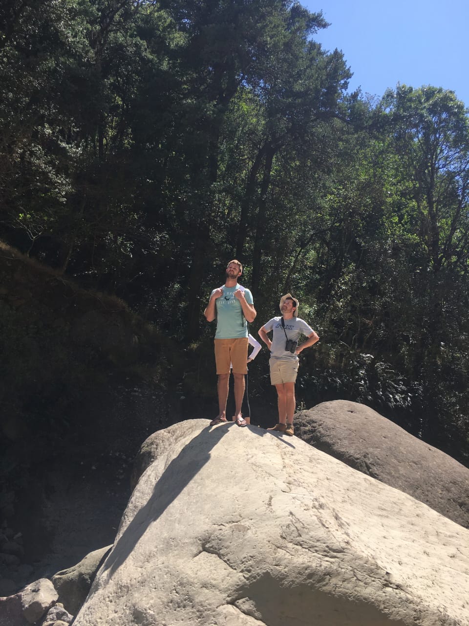 Angelo and a friend standing on a boulder in a forested gorge