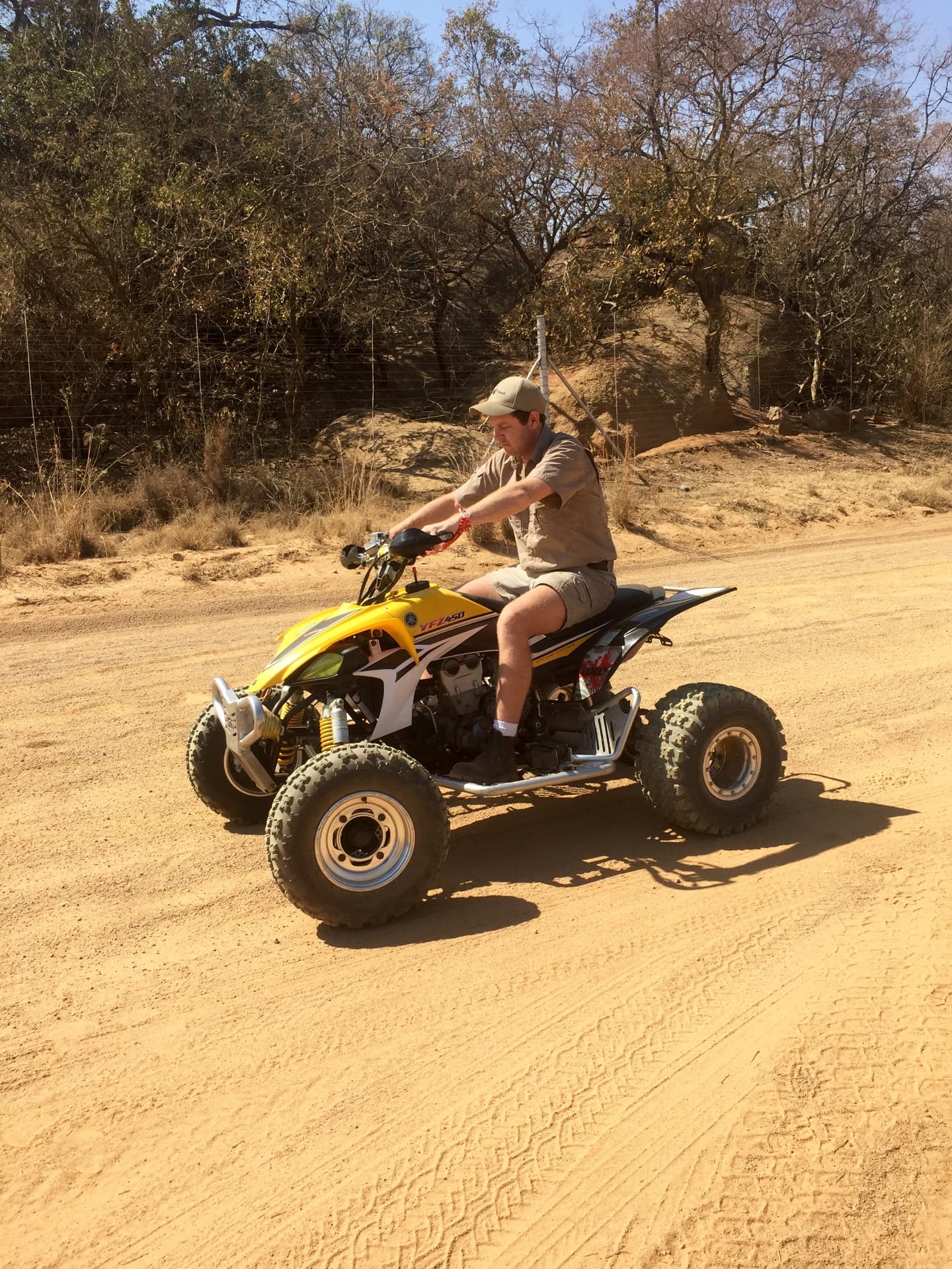 Angelo riding a yellow quad bike along a sunny dirt road