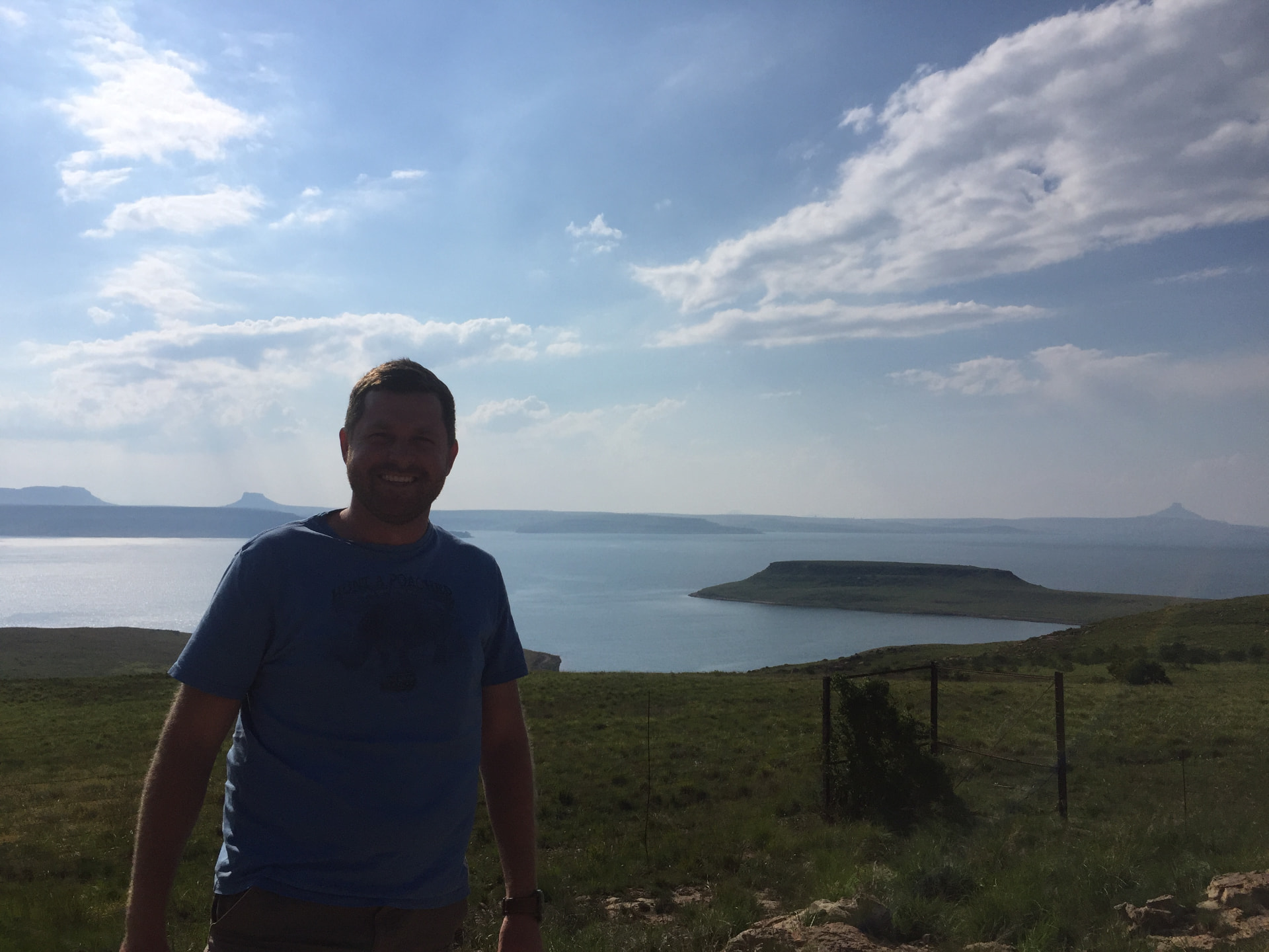 Angelo smiling on a grassy hillside overlooking the lake