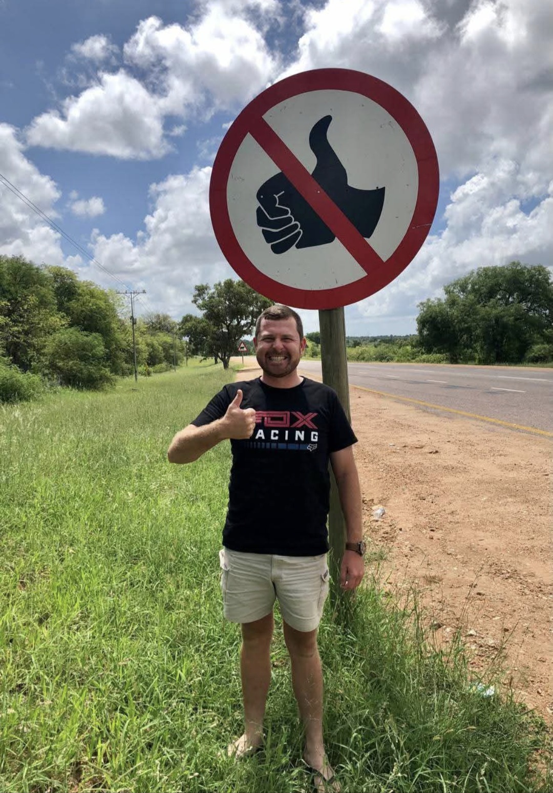Angelo giving a thumbs up beside a no-thumbs-up road sign, smiling