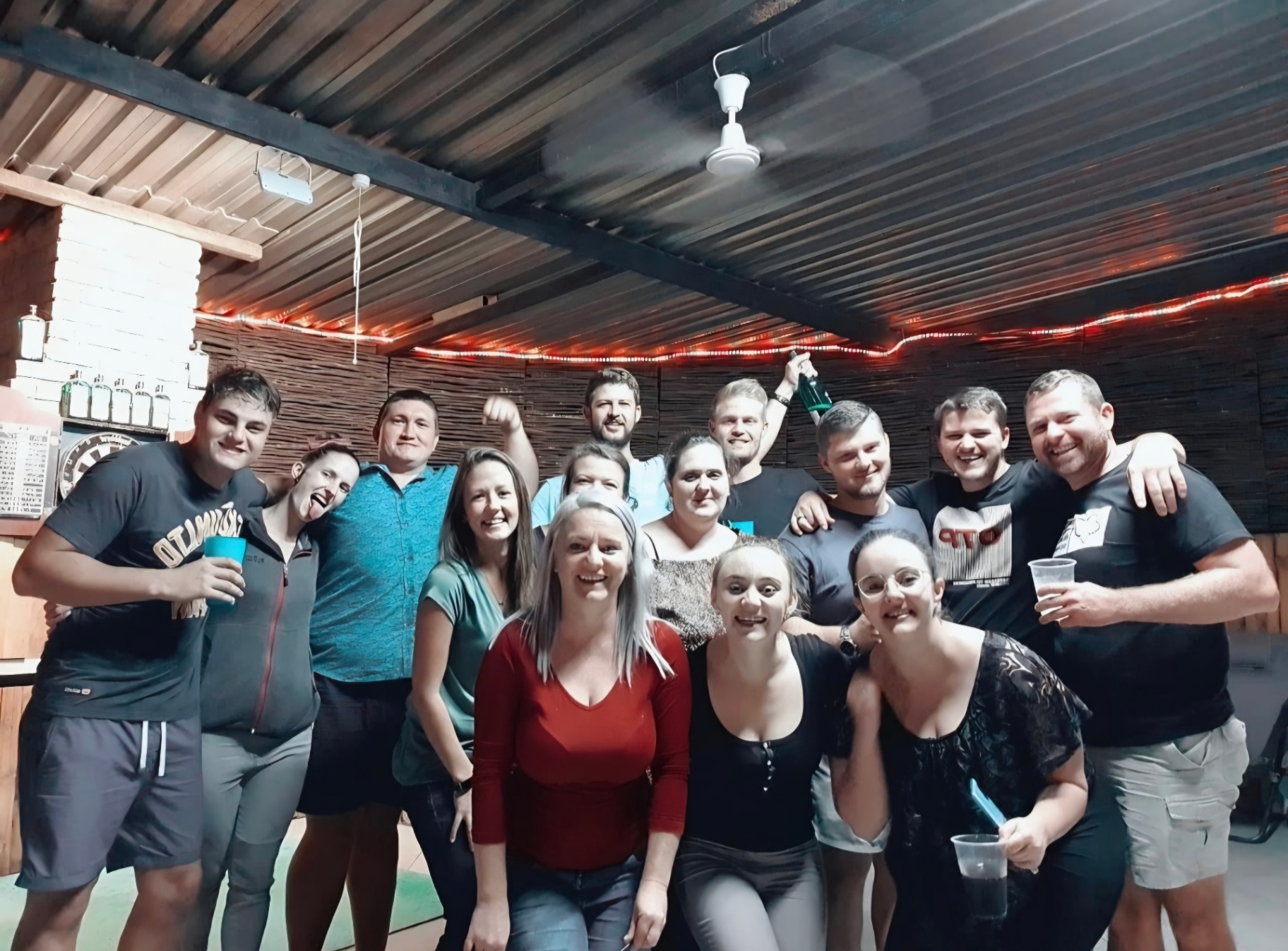A large group of friends laughing together under a lapa with fairy lights