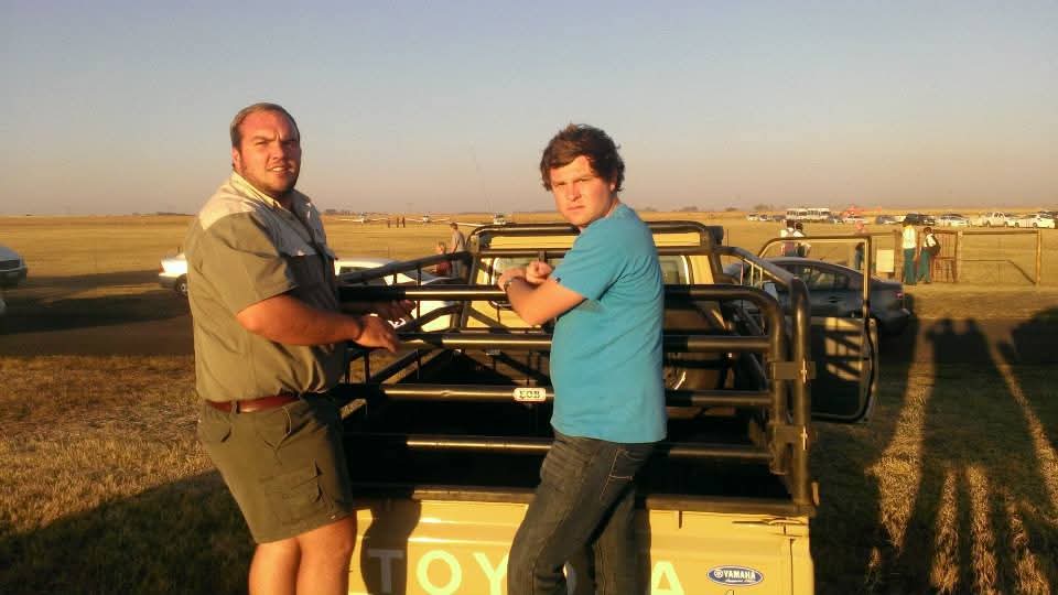 Two friends leaning on a game-viewing vehicle at sunset on the plains