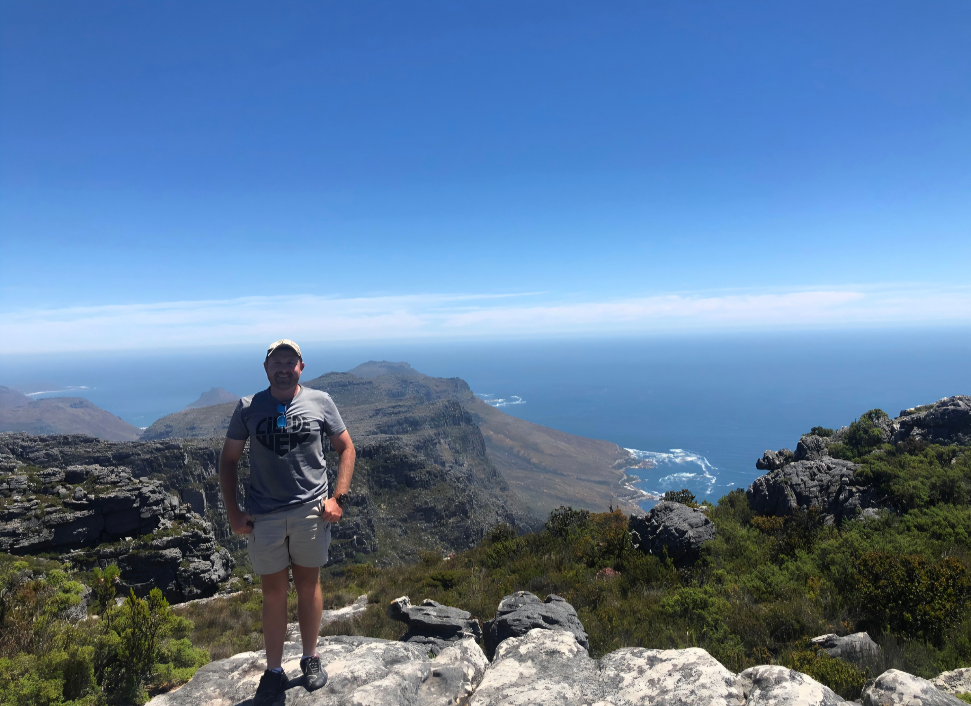 Angelo standing on a rocky mountain summit with a panoramic ocean coastline behind him