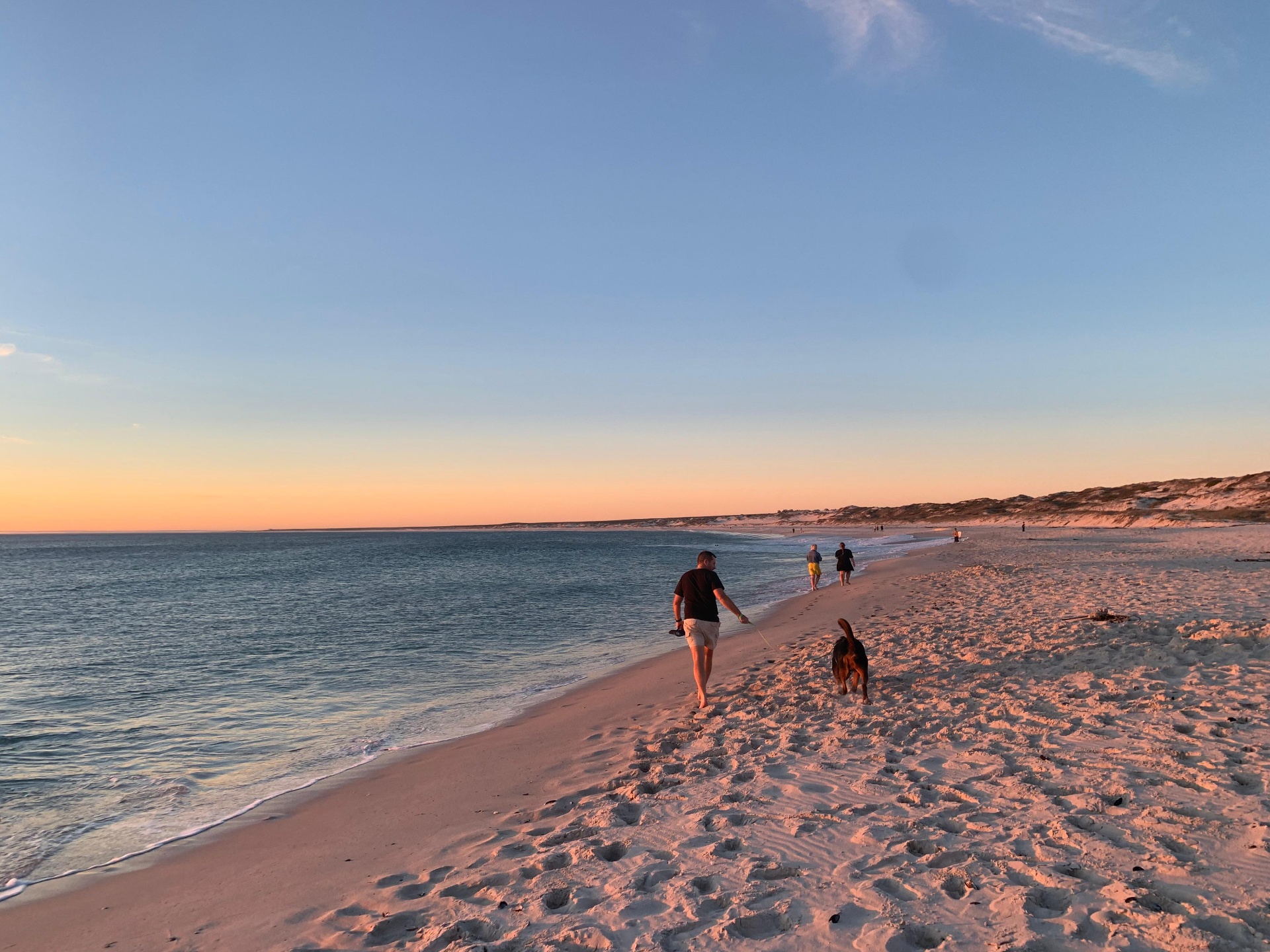 Angelo walking with a dog along a sandy beach in the warm evening light