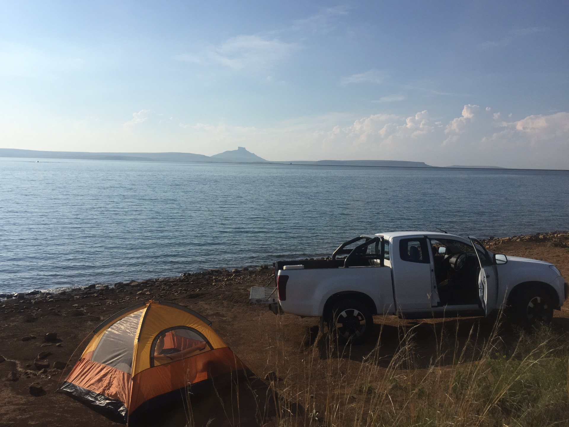 A tent and white bakkie at a campsite beside a wide blue lake