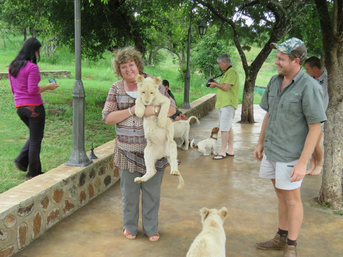 A family member holding a white lion cub while Angelo smiles nearby in a green work shirt