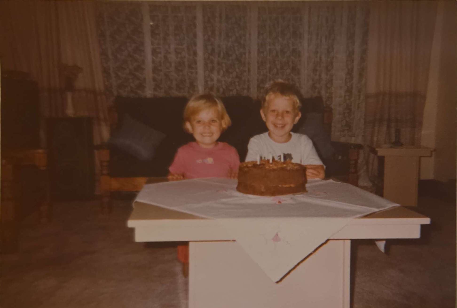 Angelo and his sister as small children smiling behind a birthday cake