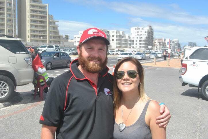 Angelo in a red cap smiling with Anzelle beside a sunny seaside street