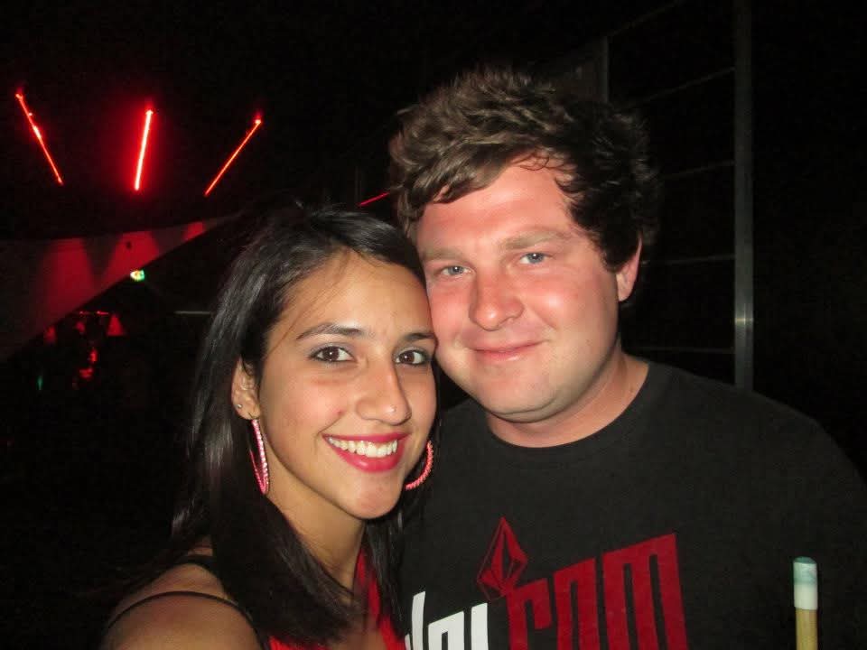 Angelo and a friend smiling together on a night out under red club lights