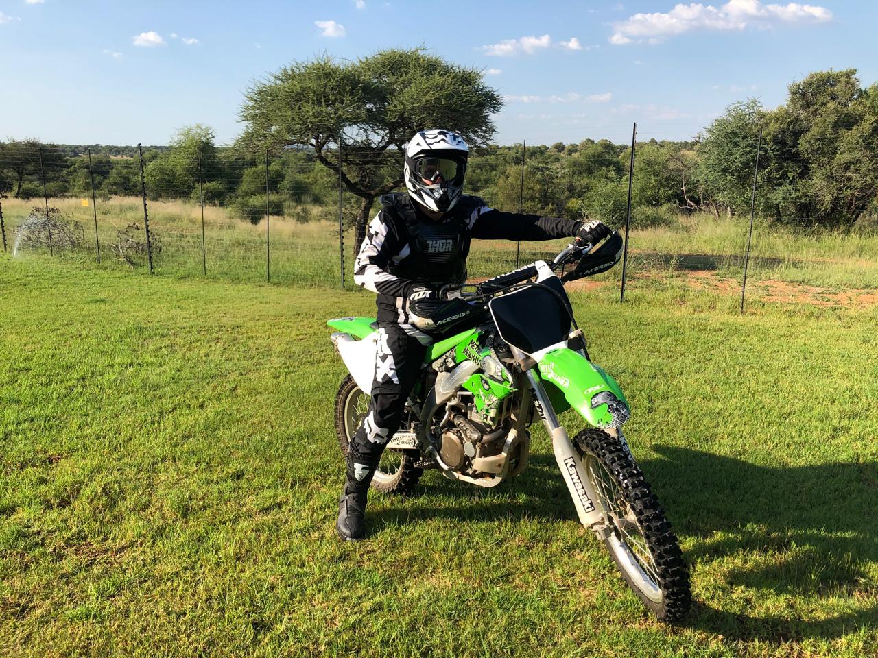 Angelo seated on his green Kawasaki dirt bike in full motocross gear