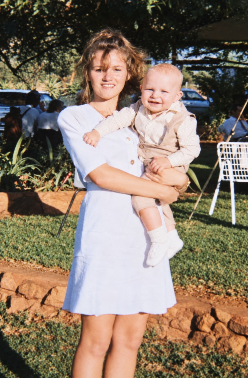 Tannie Dina holding baby Angelo, a smiling little blond boy, on a sunny lawn