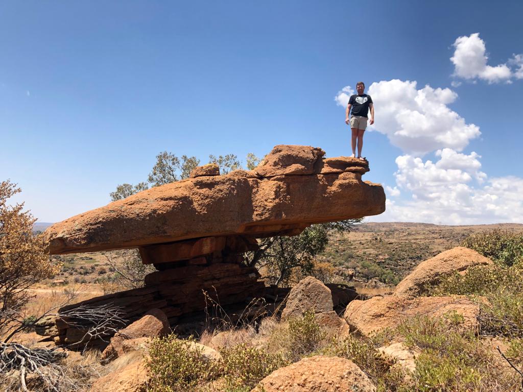 Angelo standing on a large balancing rock formation under a blue sky