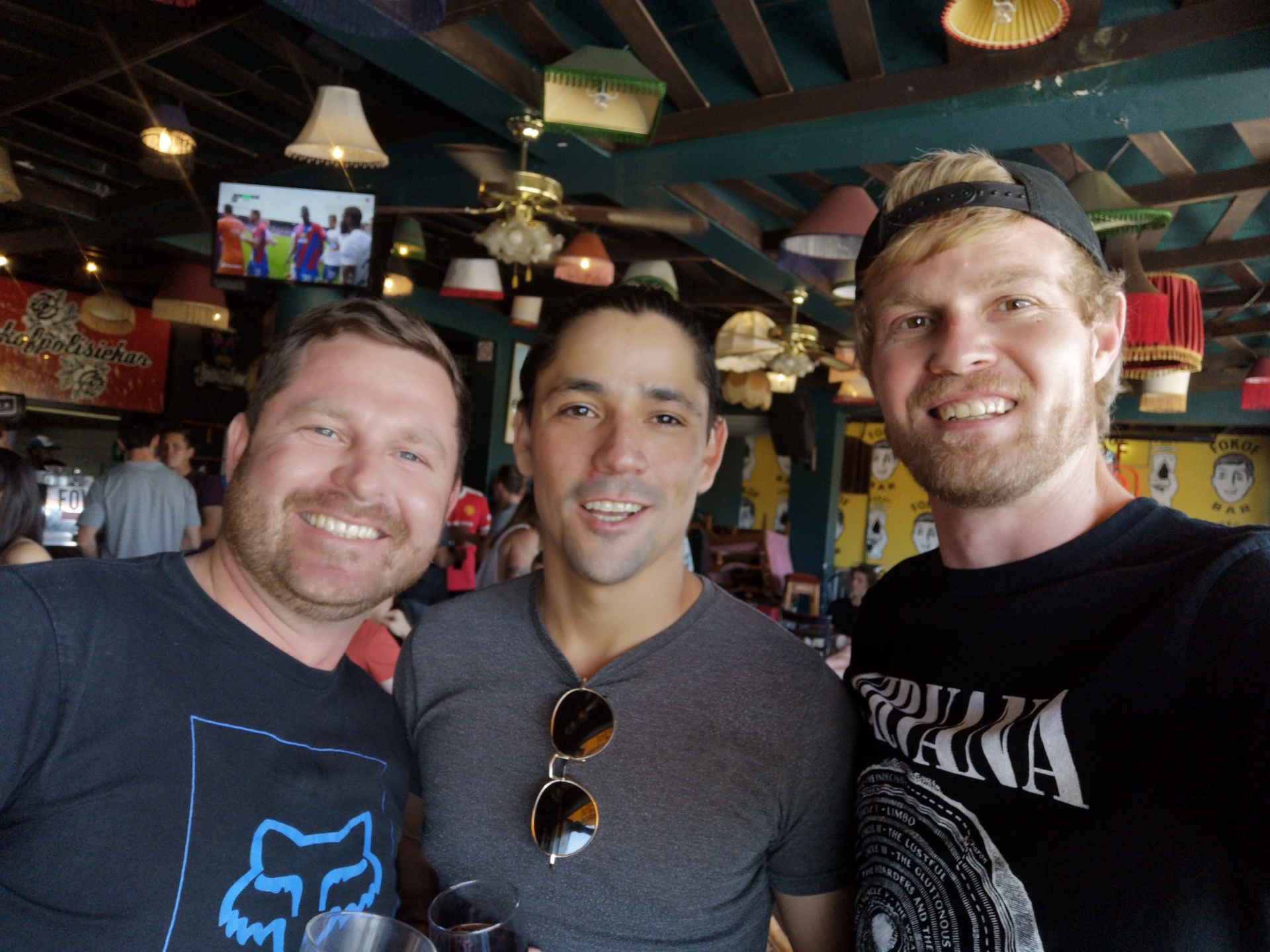 Angelo and two friends smiling together in a lively bar