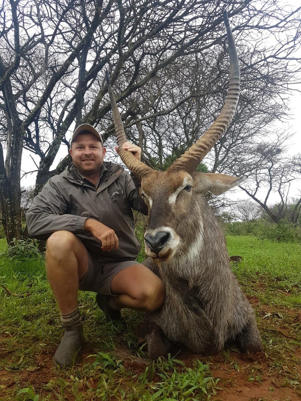 Angelo kneeling beside a waterbuck bull among winter trees