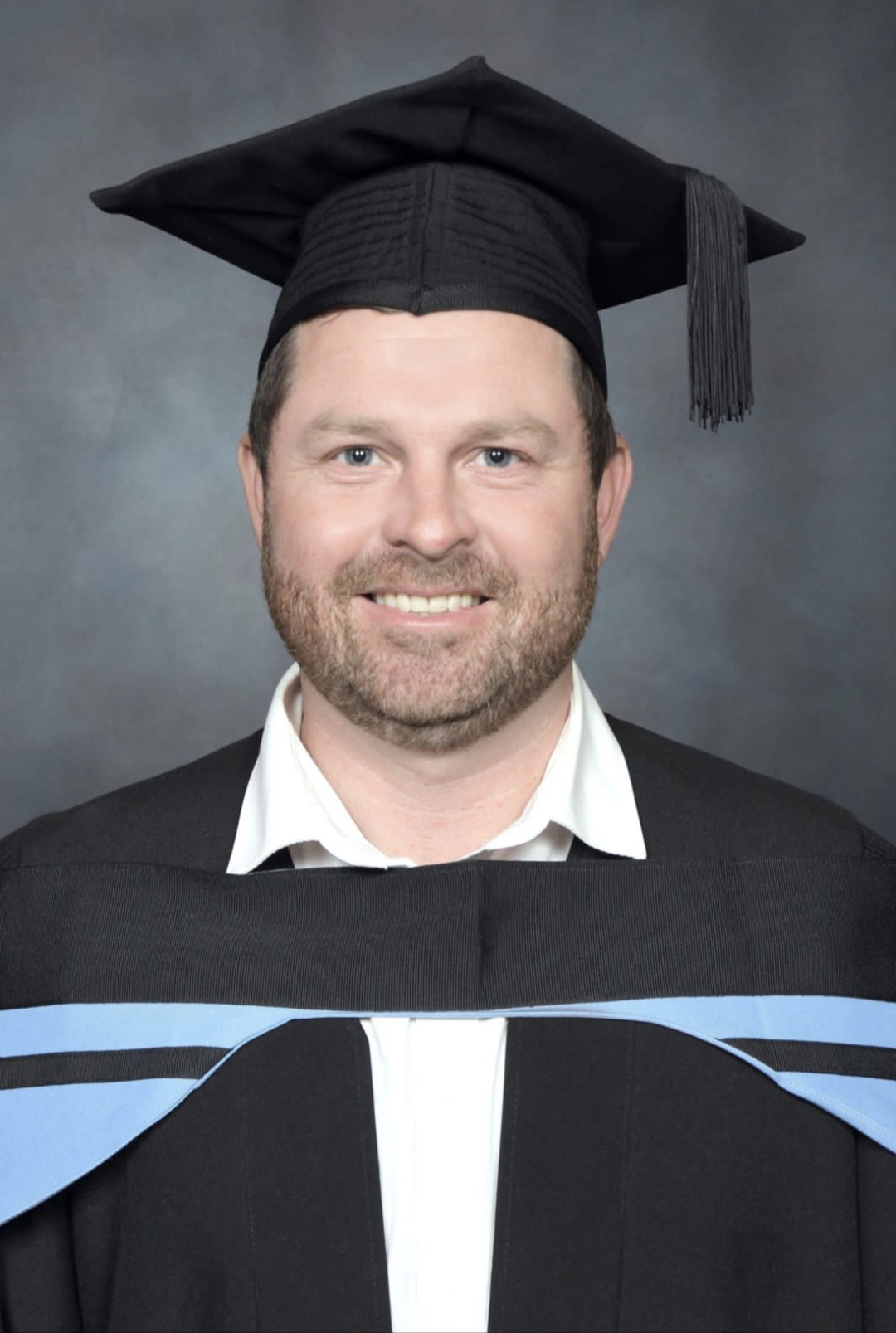 Angelo in a graduation cap and gown, smiling in a formal portrait