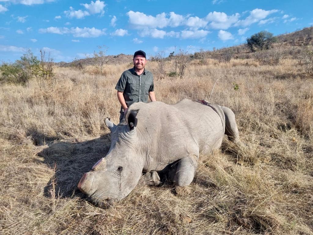 Angelo standing behind a white rhino lying down in the open grass