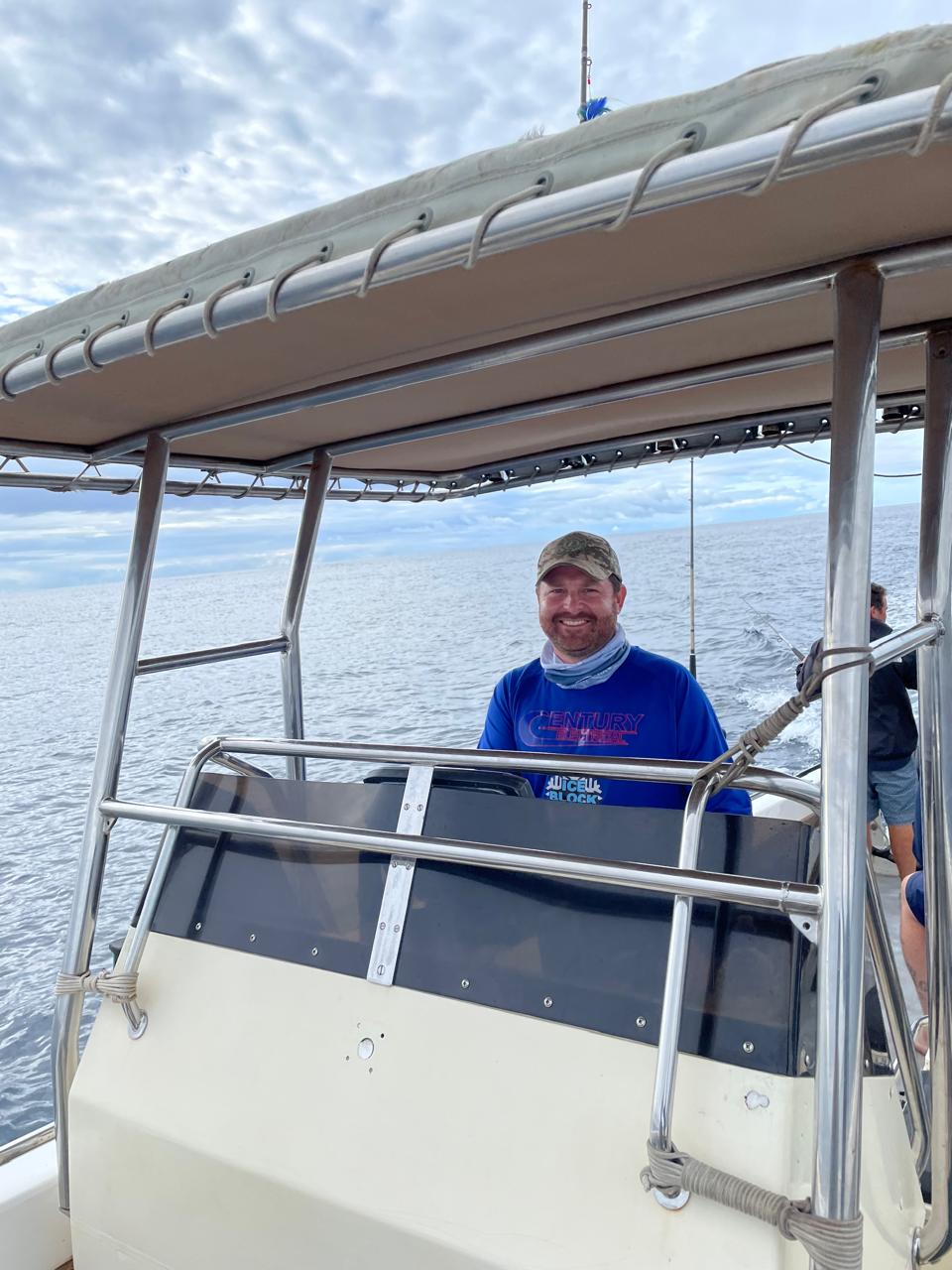 Angelo grinning at the wheel of a boat under a cloudy sky