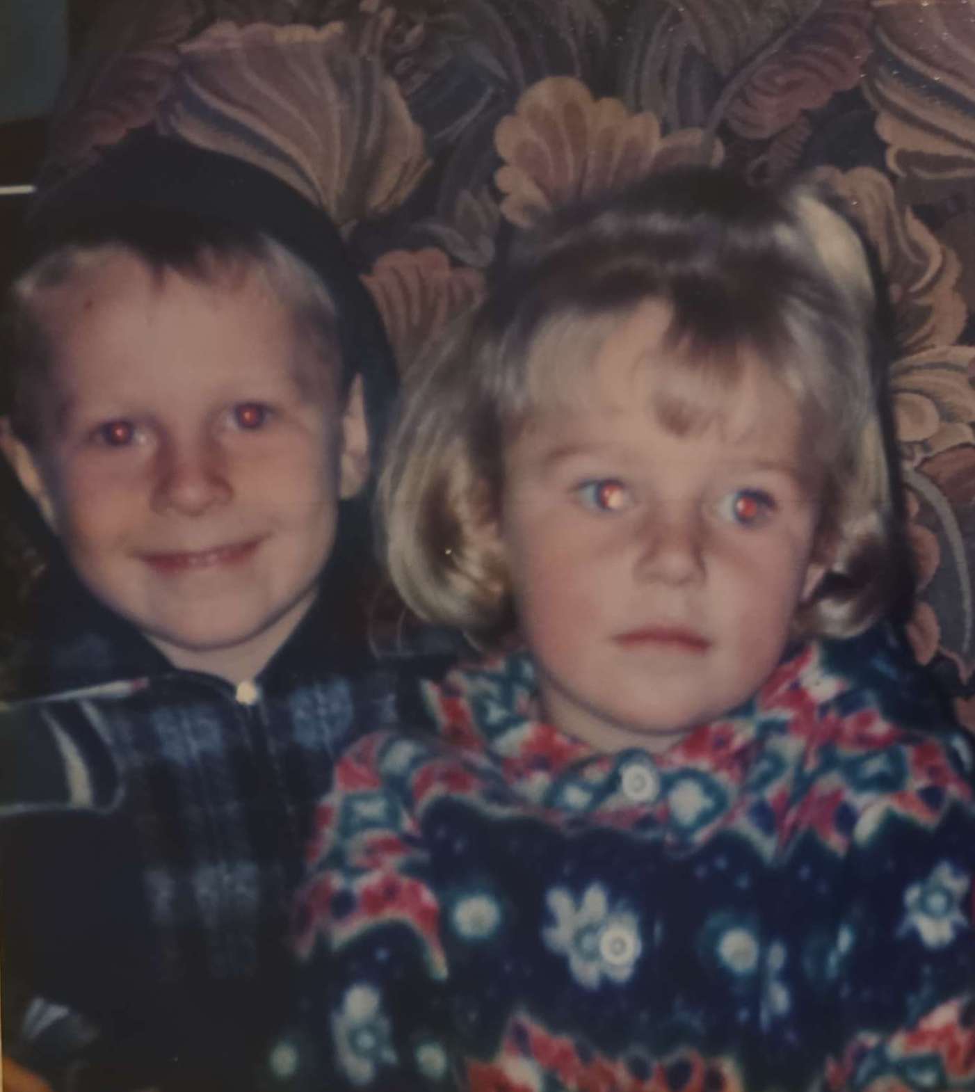 Angelo and his sister as toddlers sitting close together on a couch