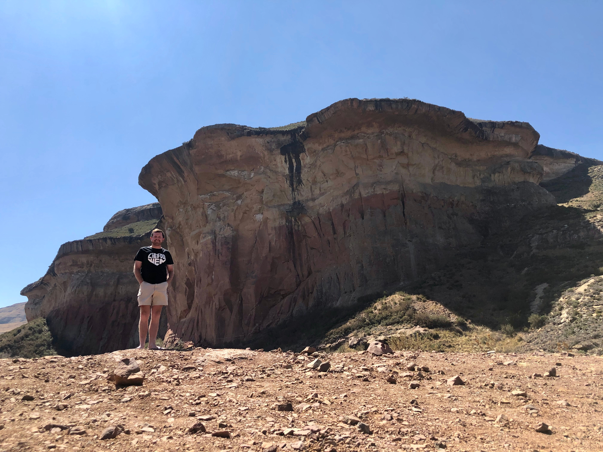 Angelo standing barefoot before towering layered sandstone cliffs